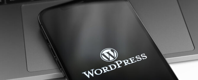 WordPress logo on screen smartphone, iPhone with notebook MacBoo